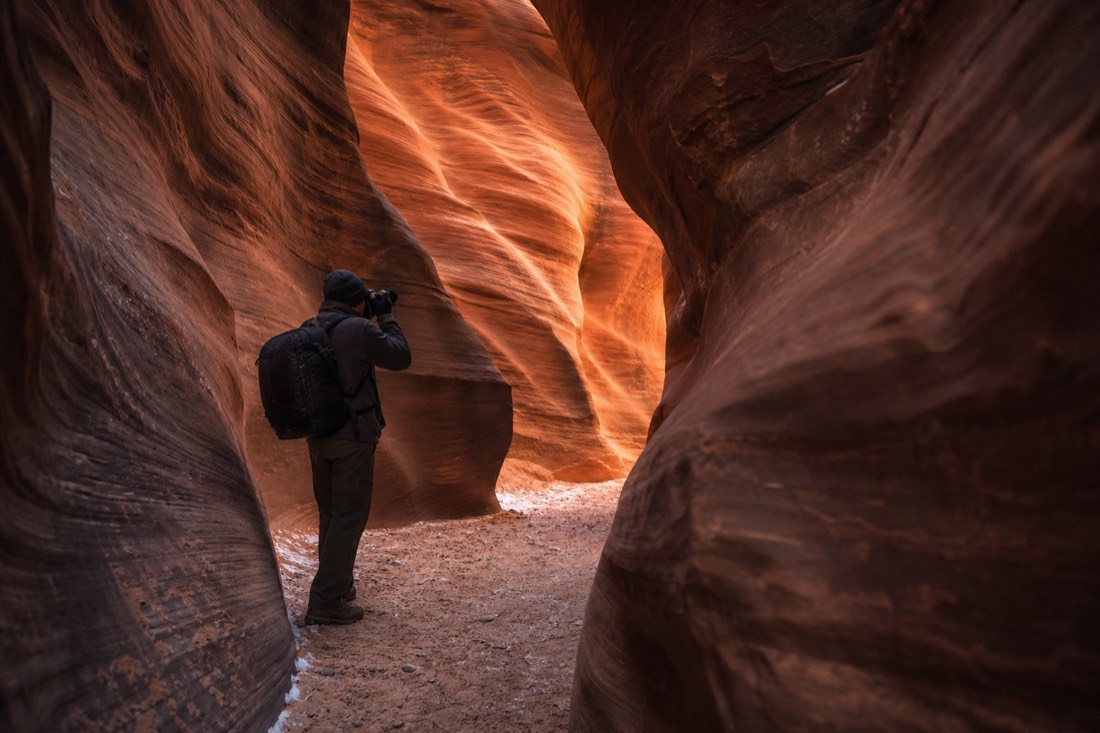 Photographer alone in a winter slot canyon framing a shot of glowing curved walls
