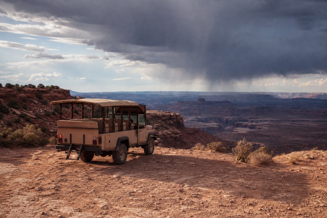 Tour guide looking at distant storm clouds from a dusty staging area outside a canyon