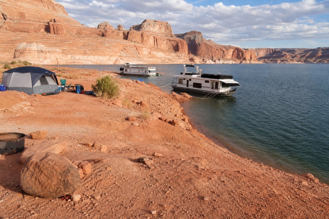 Campground beside blue lake water with red sandstone shoreline and moored boats