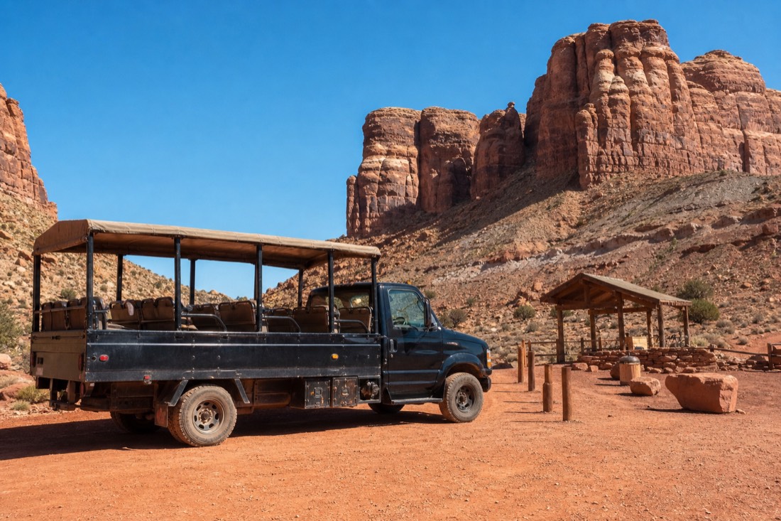 Tour vehicle parked at a dusty desert check-in area under a bright blue sky