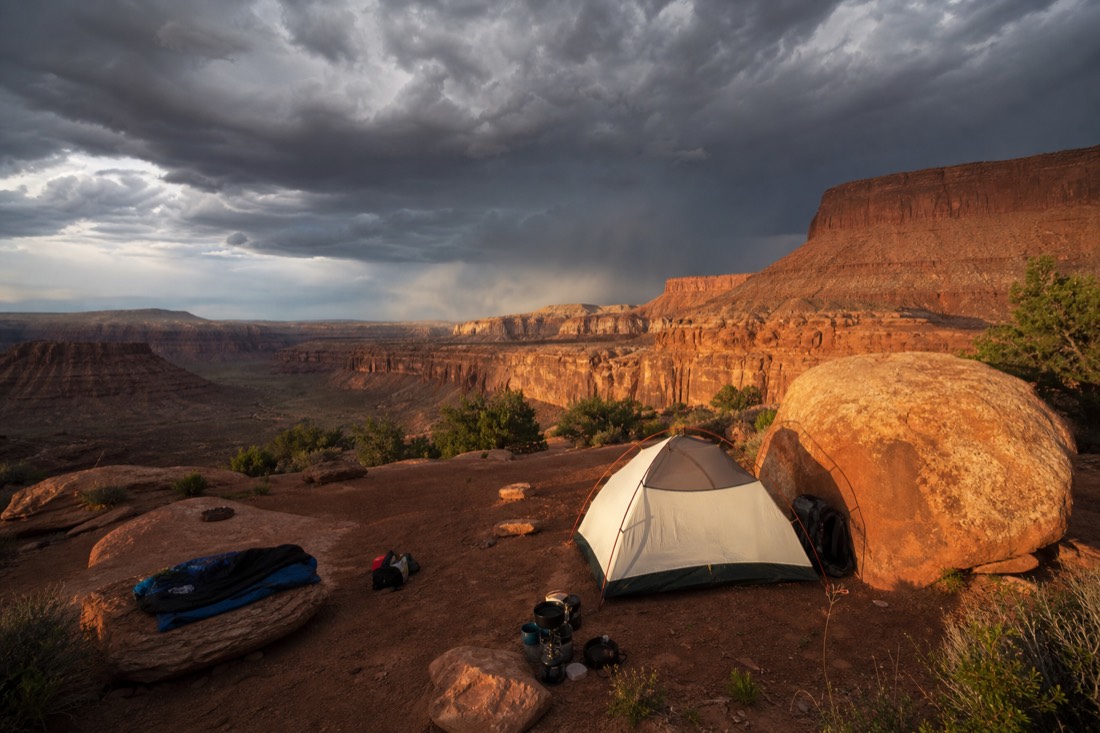 Storm clouds building over desert cliffs with a campsite in the foreground