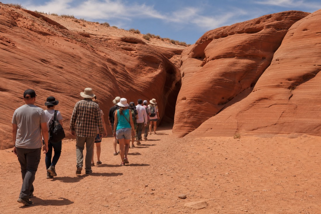 Line of visitors walking into the wide entrance of Upper Antelope Canyon under a midday sky