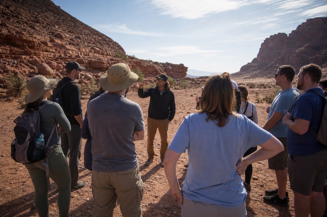 Small tour group gathered around a guide at a scheduled departure point in the desert
