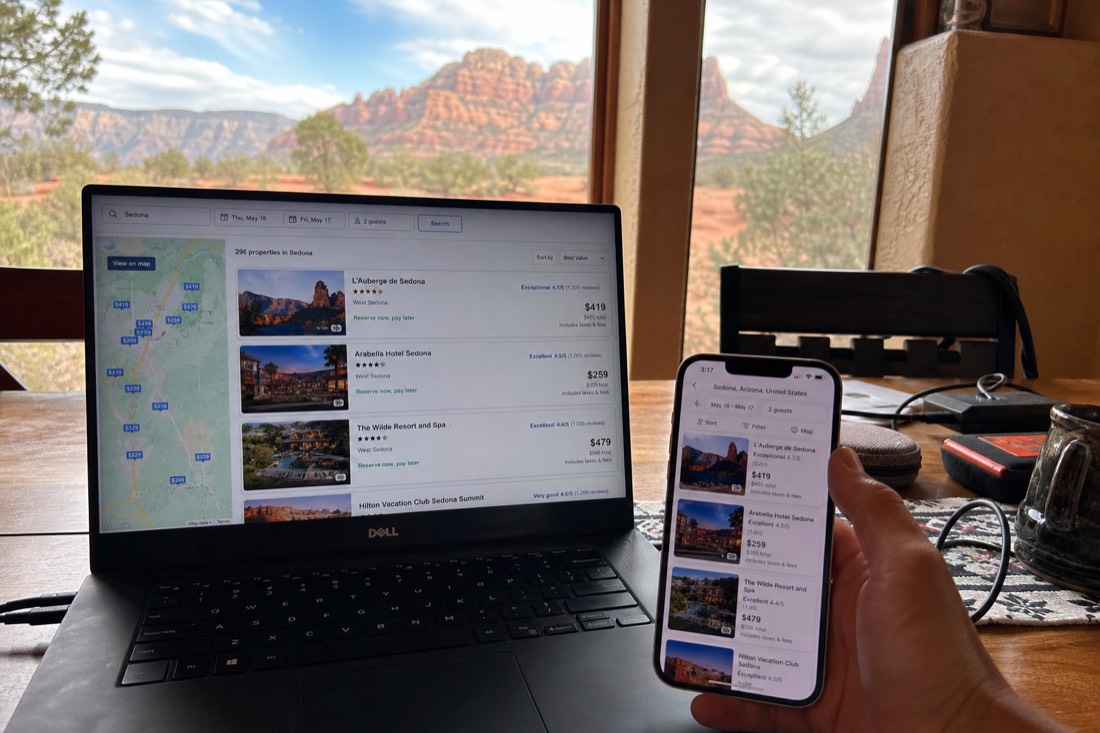 Person comparing two booking pages on a laptop and phone at a kitchen table