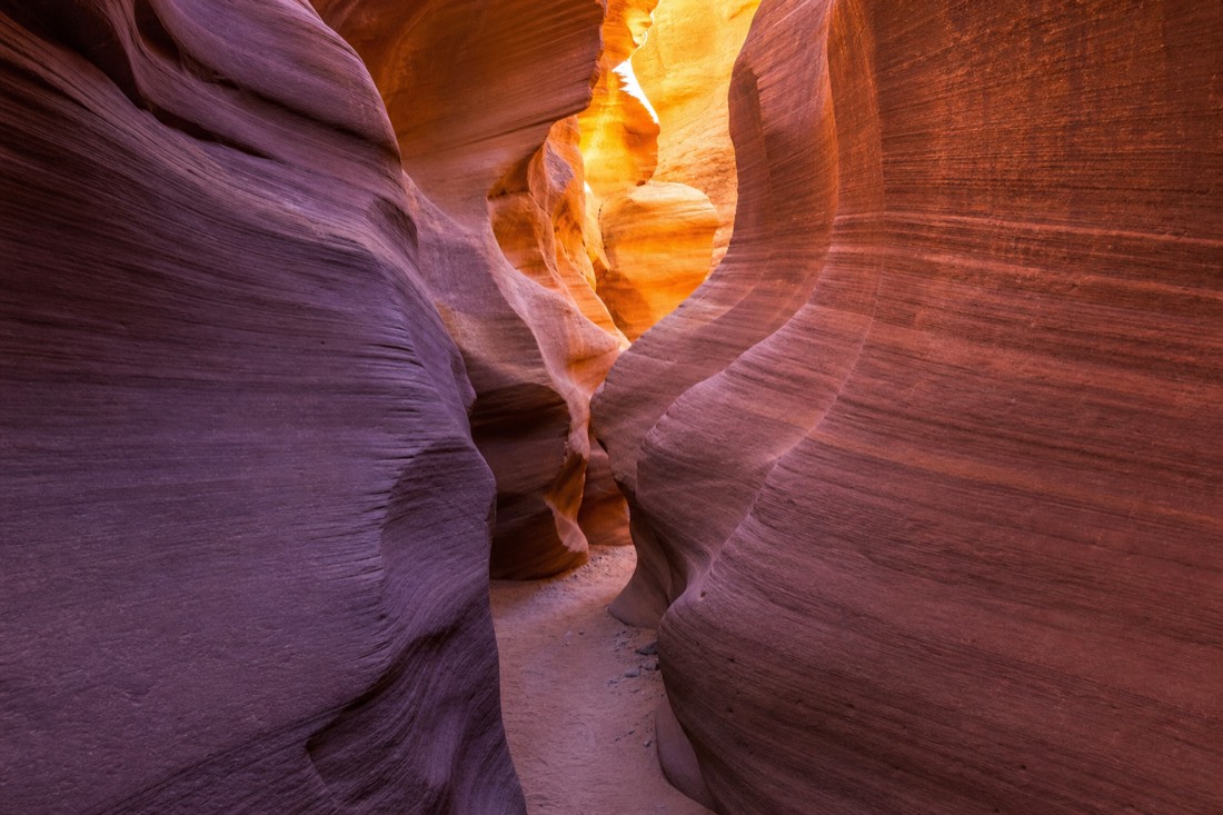 Sunlight bouncing between curved canyon walls creating glowing gradients of orange and purple