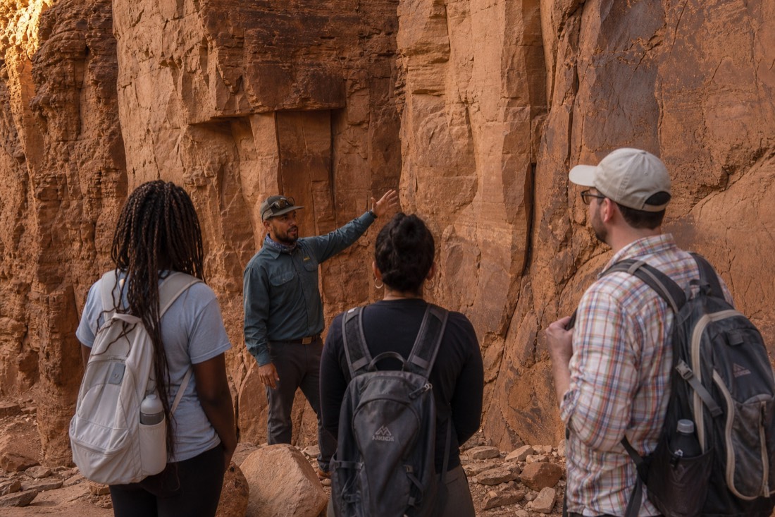 Guide gesturing toward canyon walls while a small group listens in soft light