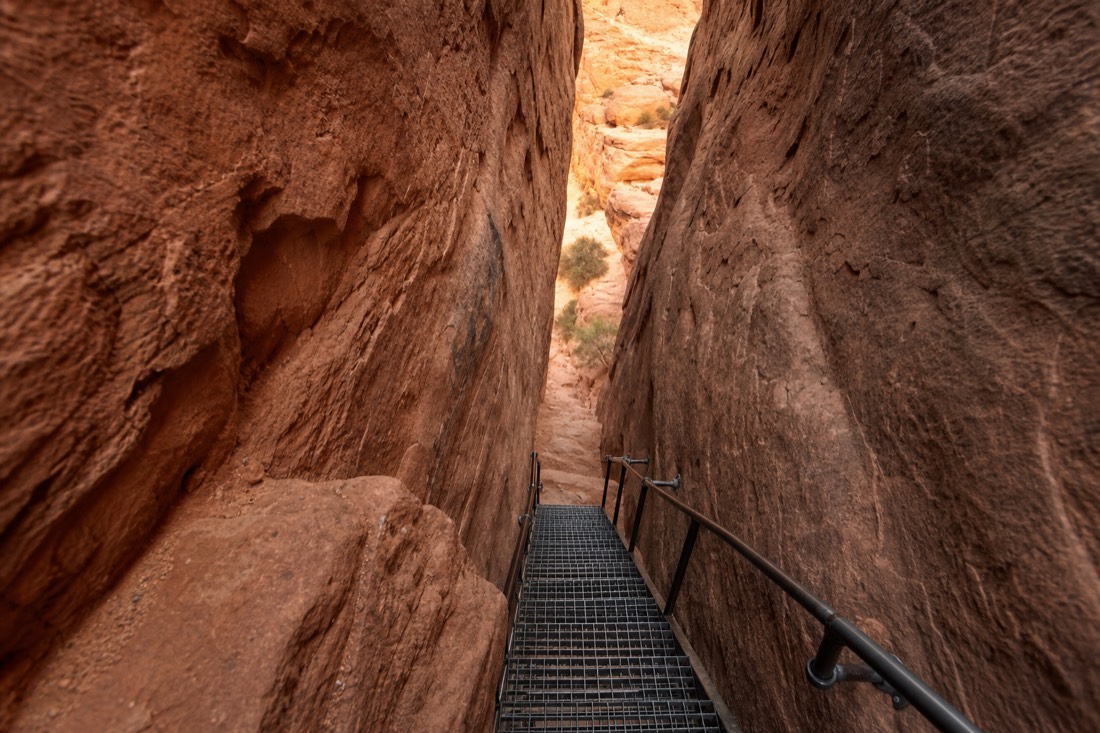 Steep metal staircase bolted into narrow sandstone walls descending into a slot canyon