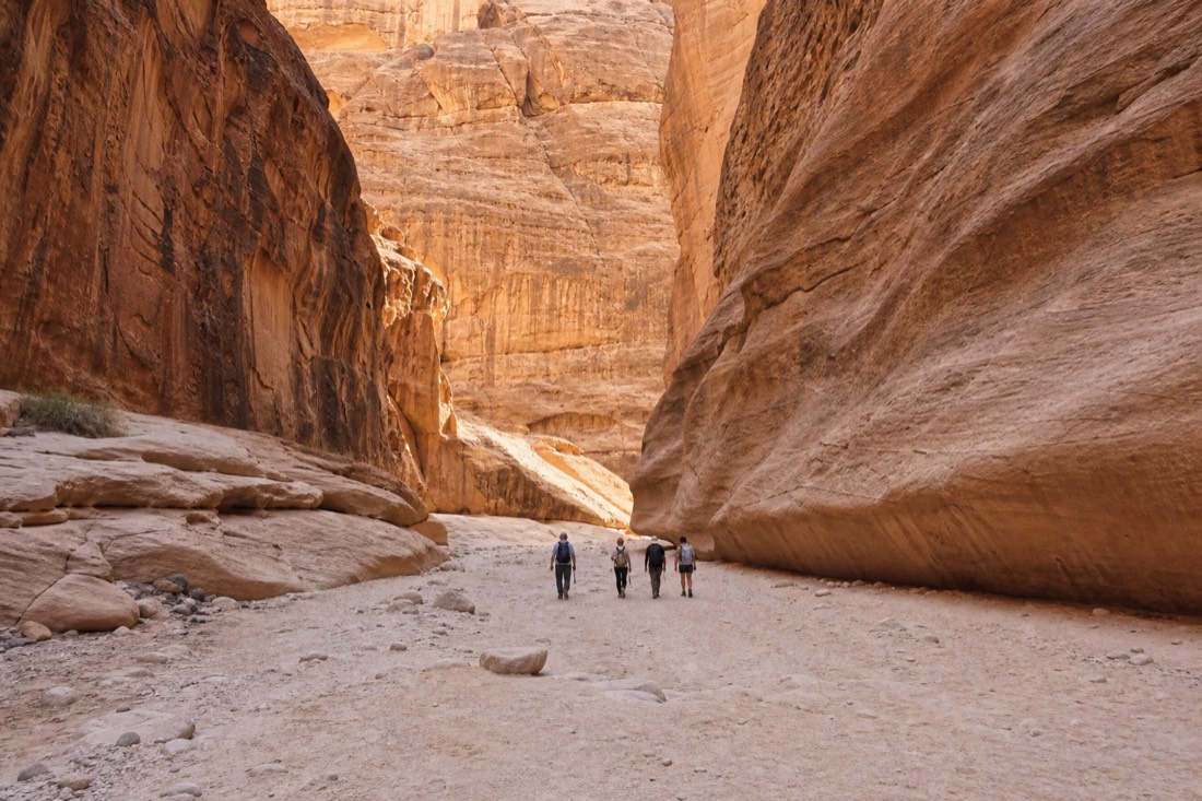 Wide sandy canyon floor with towering smooth walls and a small group walking through