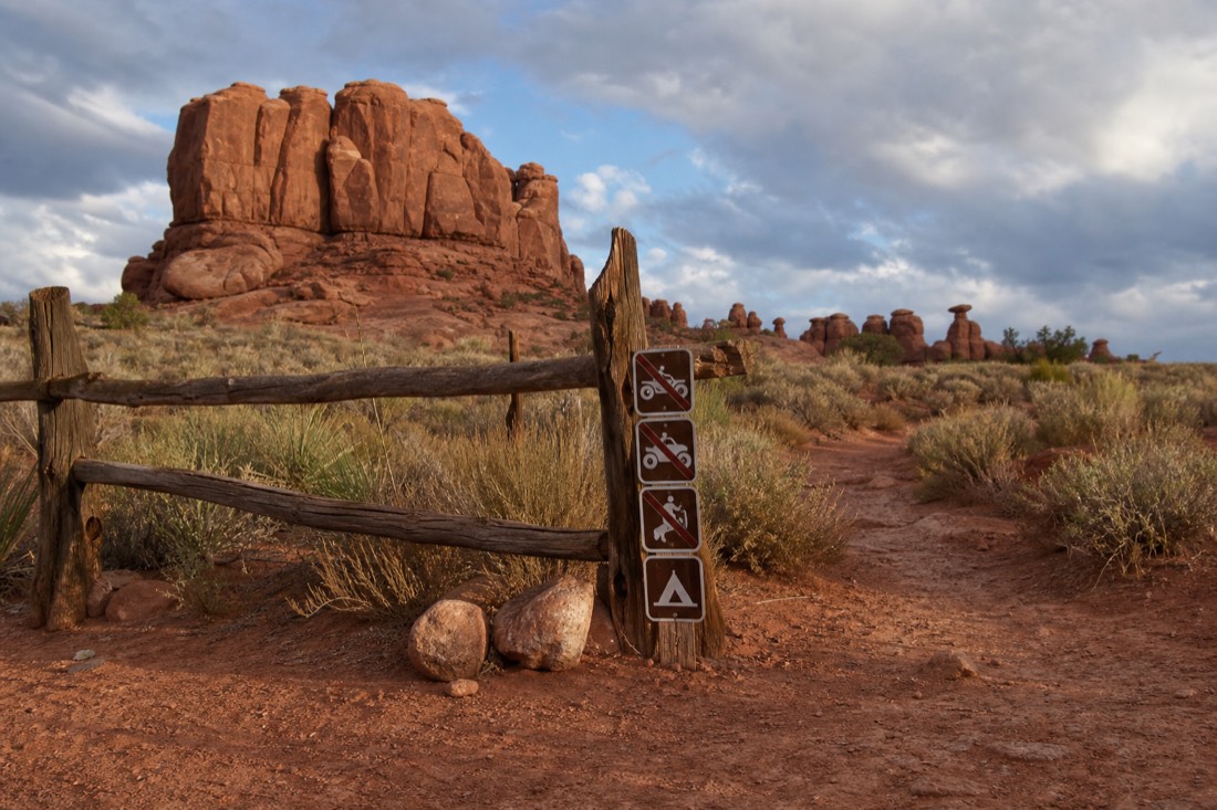 Wooden tribal park boundary sign on red dirt with sandstone formations in the distance