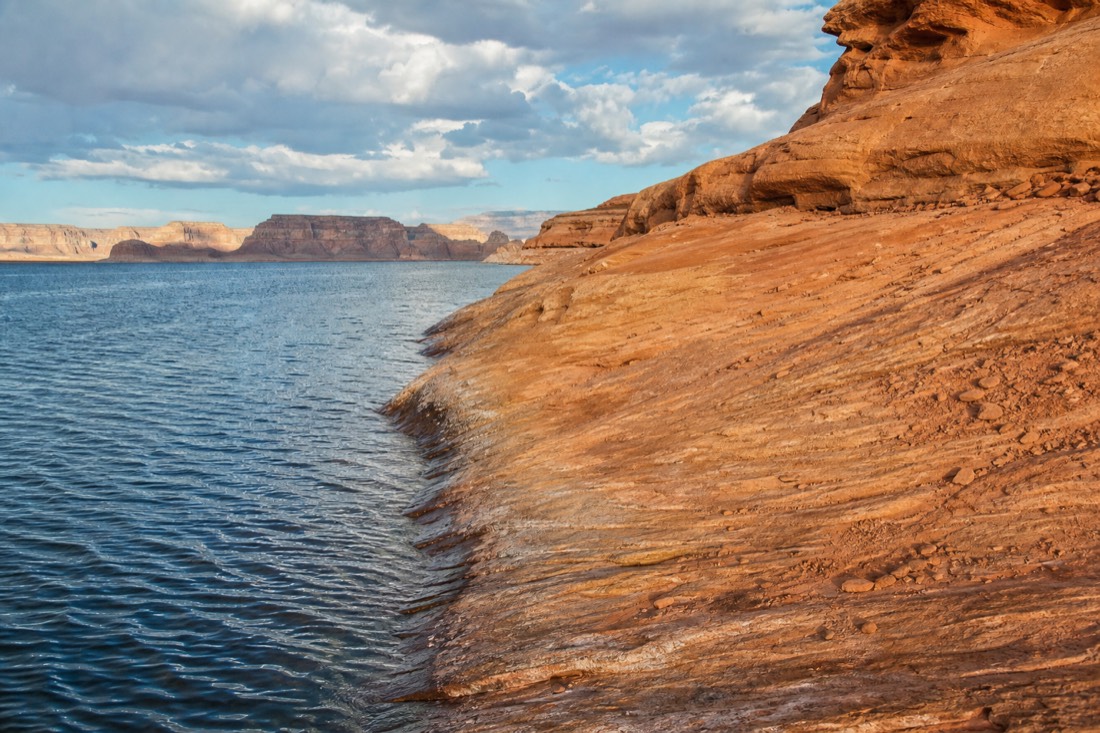 Lake Powell shoreline with blue water against orange rock under a wide desert sky