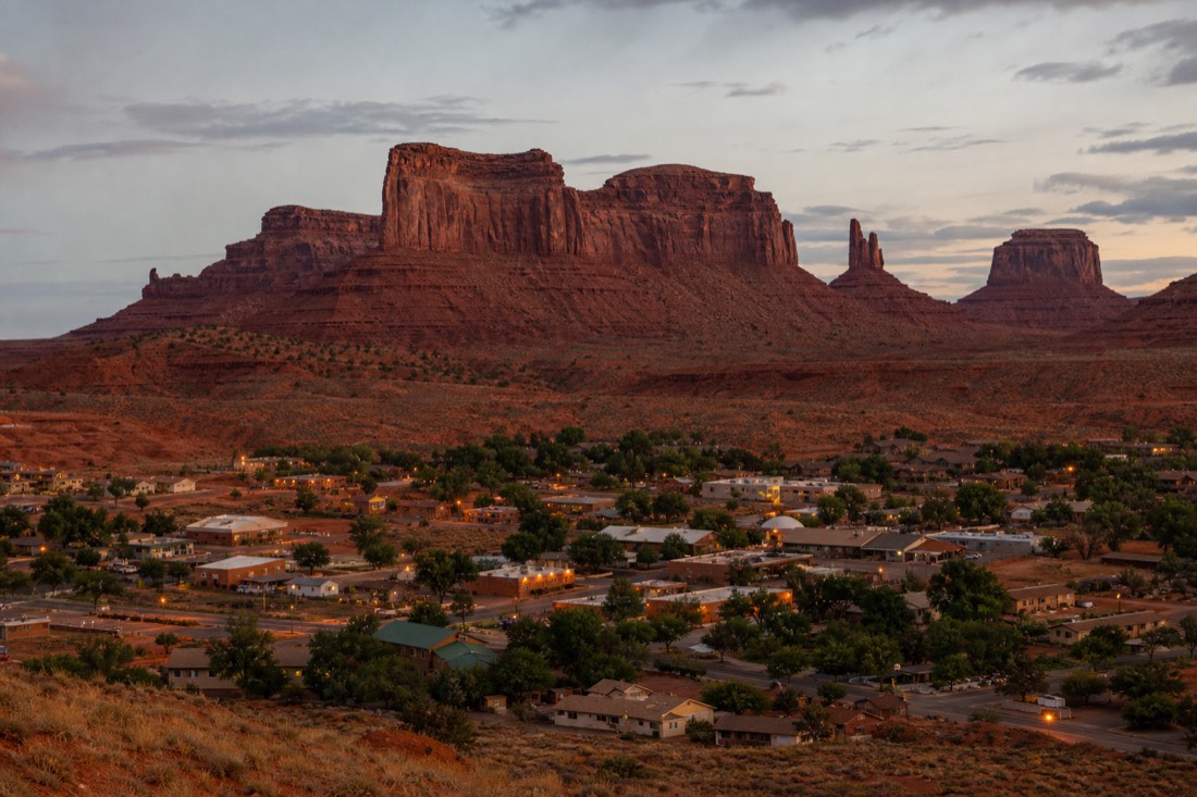 Small desert town at dusk with warm lights and sandstone mesas behind