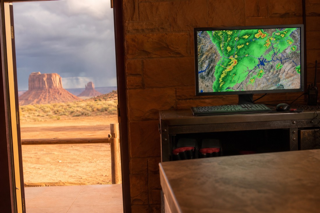 Tour operator staff watching a weather radar screen at a desert check-in office while storm clouds gather over distant mesas