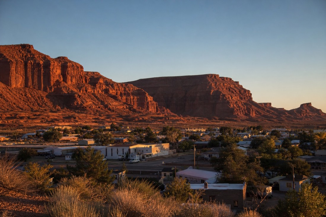 Small desert town lit at dusk with sandstone mesas behind it