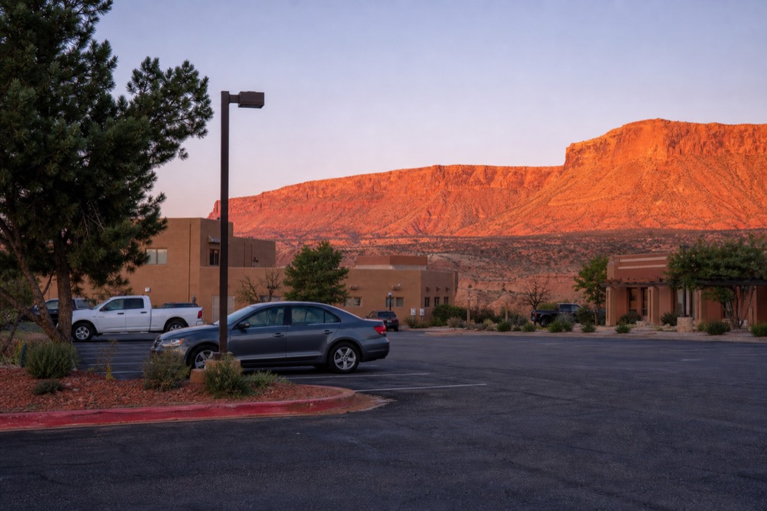 Hotel parking lot at first light in a small desert town with red mesas glowing behind