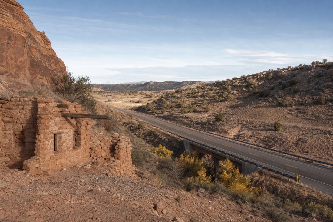 Historic stone trading post beside a two-lane highway on the Navajo Nation with a bridge over a dry wash