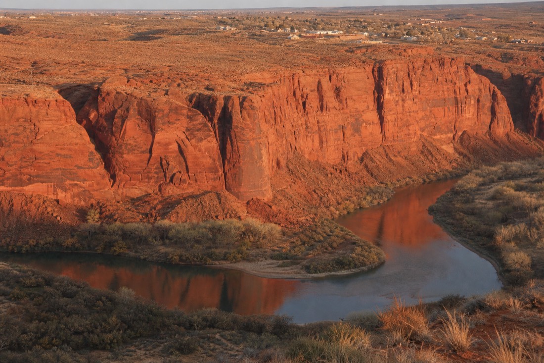 Late afternoon light on the Colorado River bend below red cliffs with a small town on the mesa behind