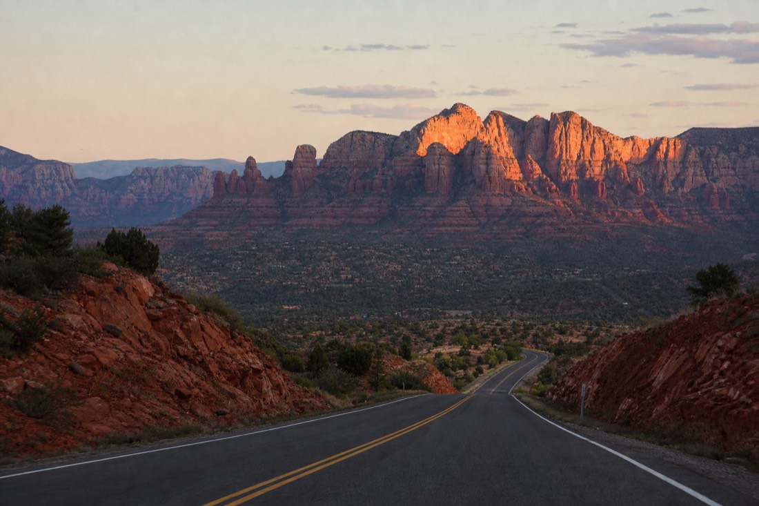 Highway at dusk descending toward red rock buttes with the last light on the cliffs