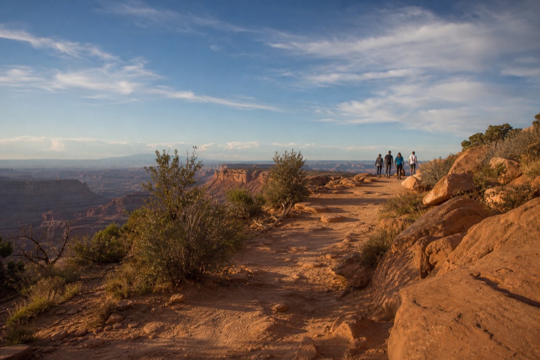 Sandy trail leading to a canyon rim overlook with visitors walking under a wide desert sky