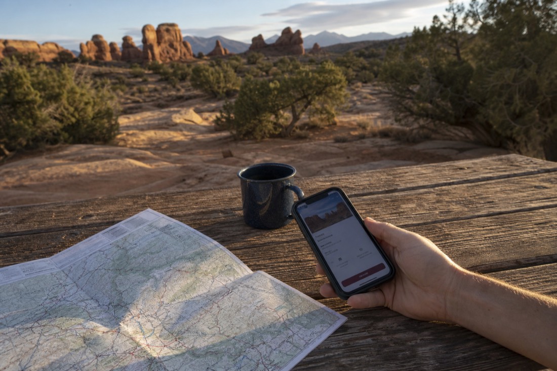 Traveler at a wooden table checking a phone booking confirmation with a road map and coffee