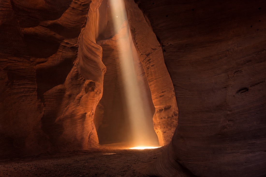 Phone held steady in two hands framing a shaft of light inside a slot canyon