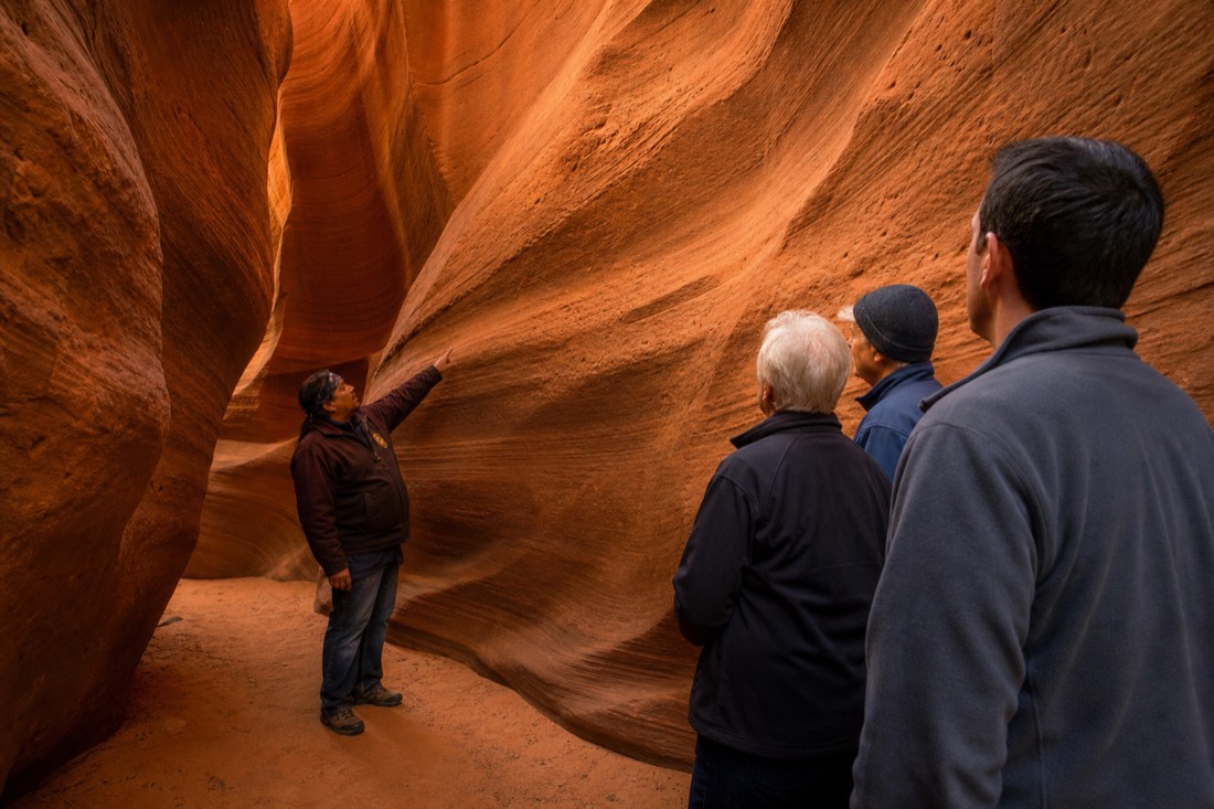 Small respectful group standing still in a slot canyon while a Navajo guide points out a wall formation, no bags or drones in sight