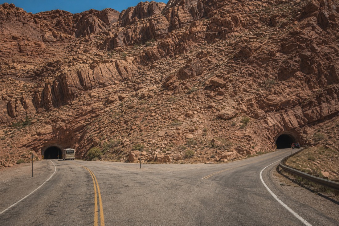 Desert highway with two turn-offs toward separate canyon entrances, tour trucks parked at each