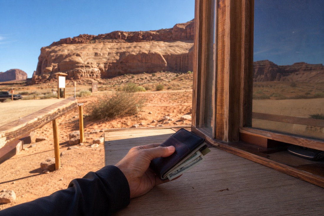 Visitor's hand holding a phone wallet and folded bills at a wooden check-in counter in the desert