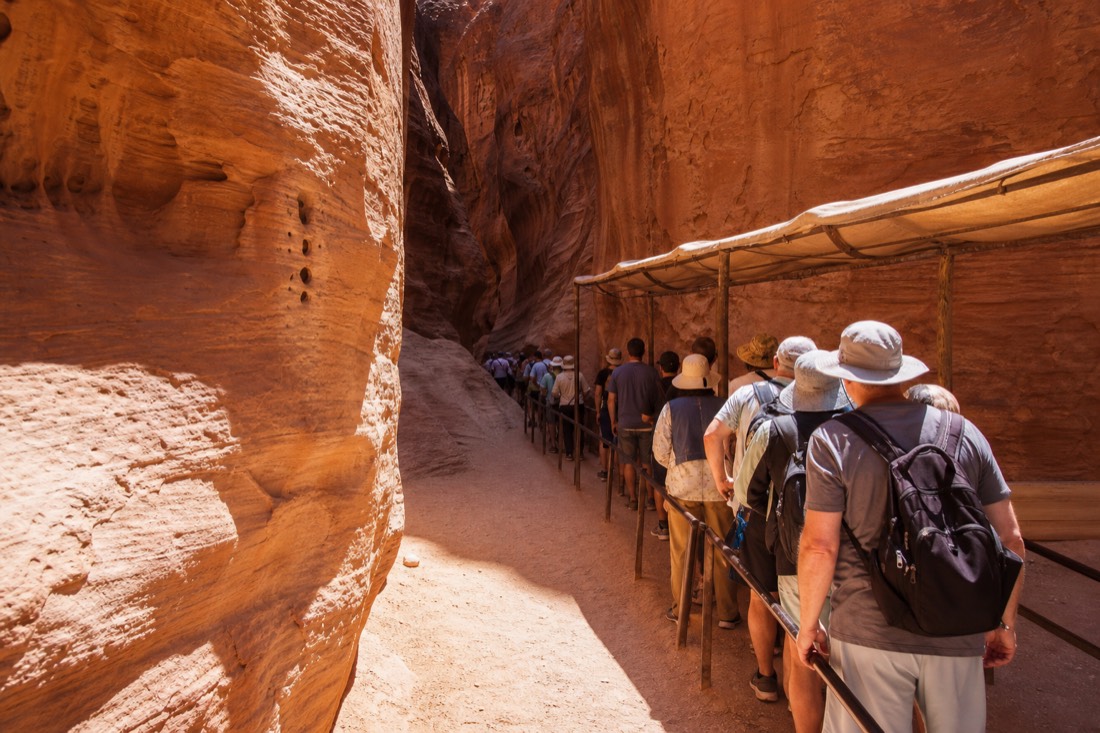 Sunlit slot canyon entrance with a short line of visitors under a shade structure in high season