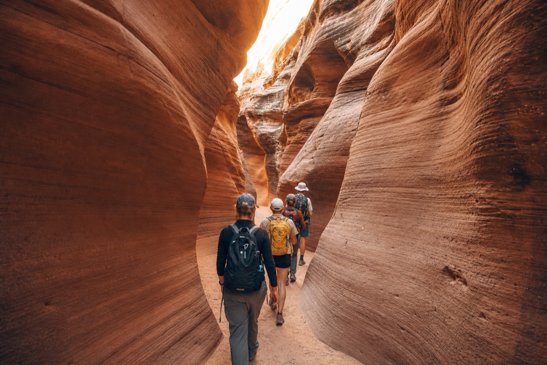 Small guided group walking single file along the sandy floor of a curving slot canyon