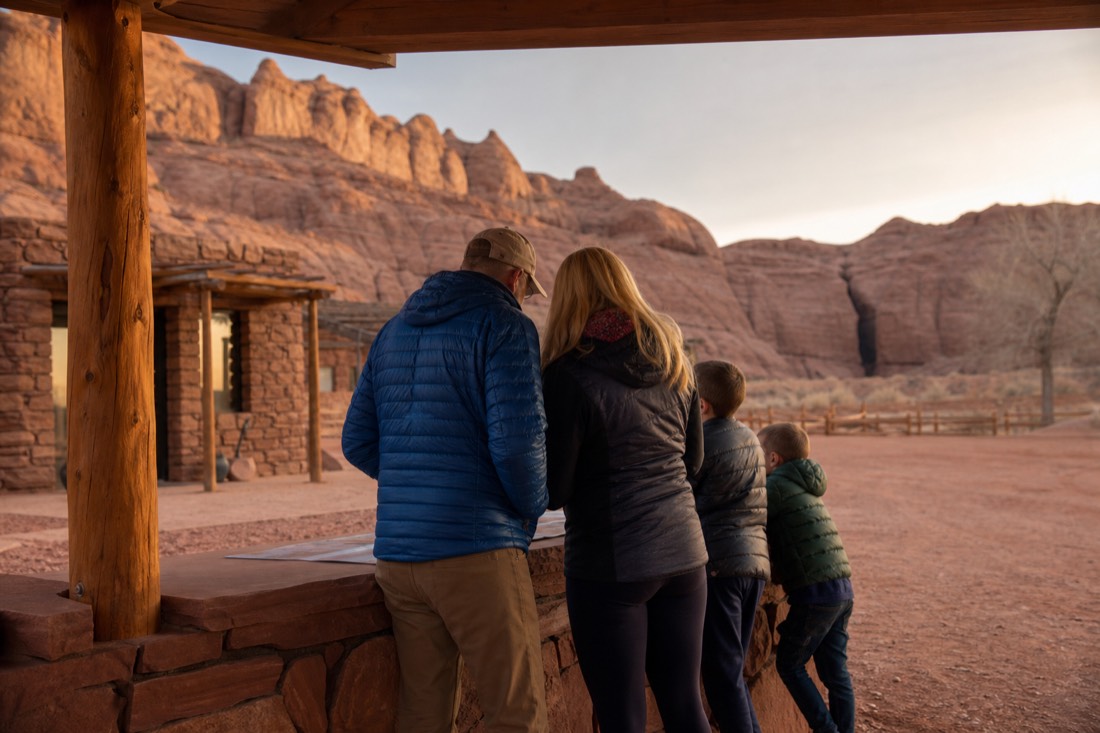 Family checking in at a desert tour office in early morning light with a slot canyon entrance in the distance