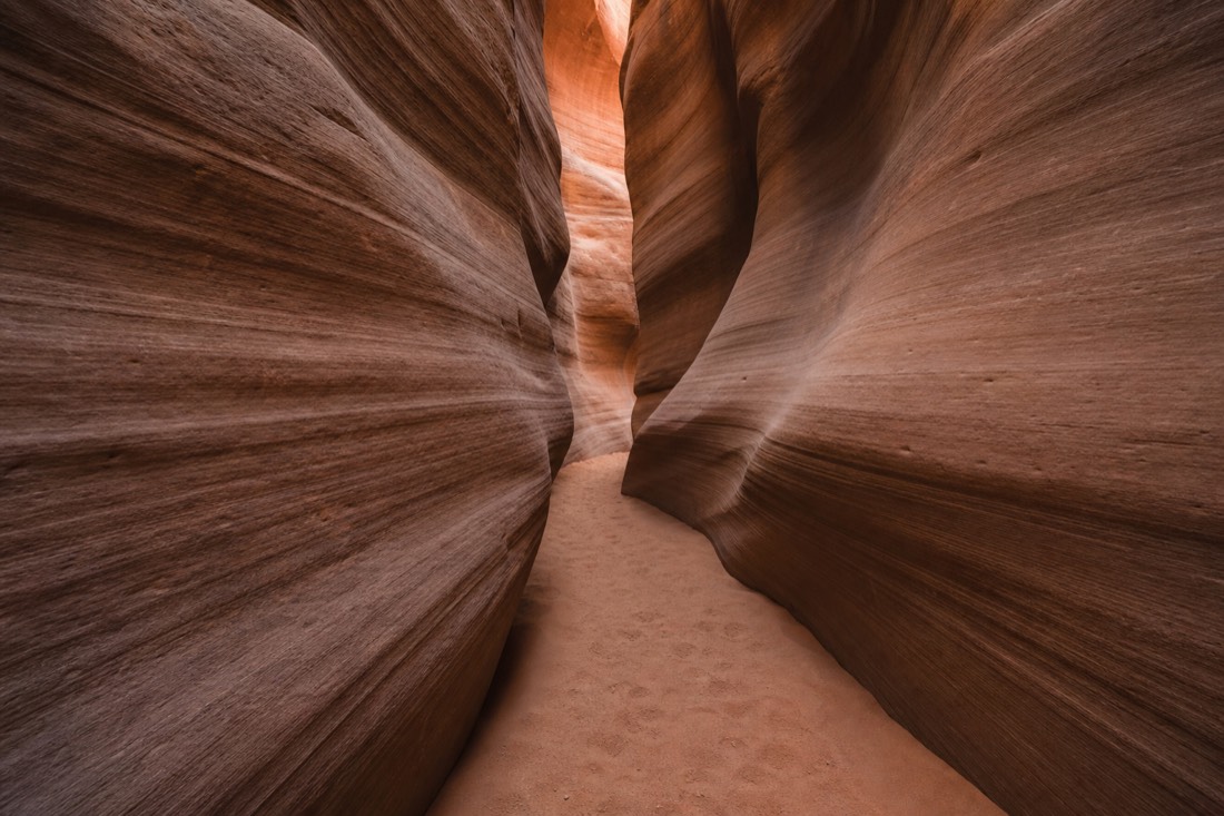 Quiet slot canyon chamber with untouched sand and layered walls, footprints only along the guided path