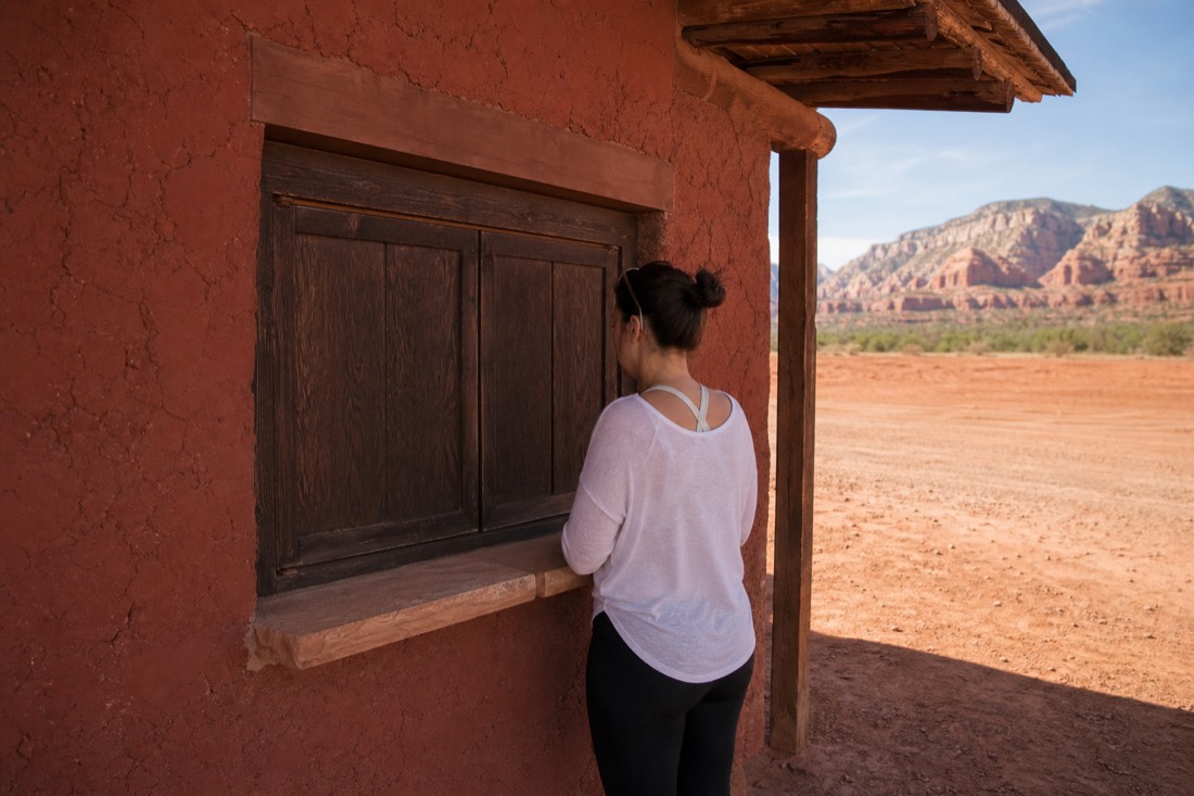Visitor standing at the closed window of a shaded desert tour office with an empty lot behind
