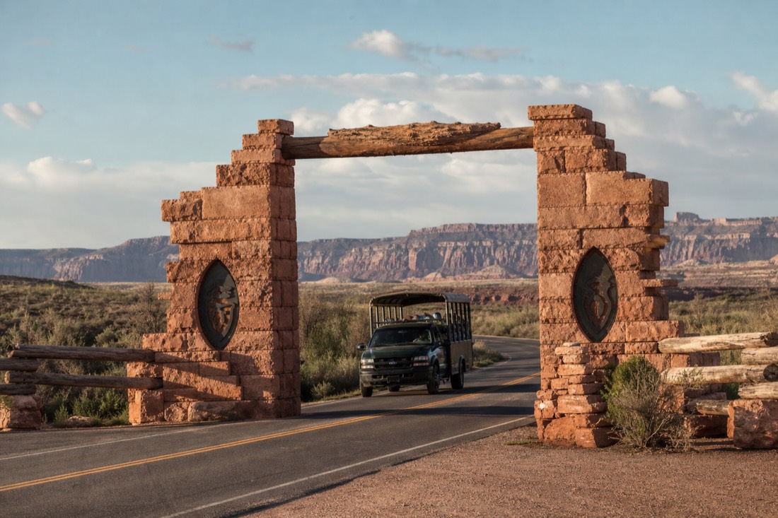 Tribal park entrance gate beside a desert road with a tour vehicle passing in warm light