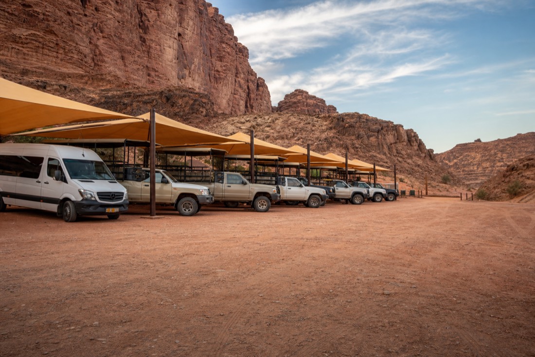 Row of shade canopies and parked tour vehicles at a dusty roadside staging area under a blue sky
