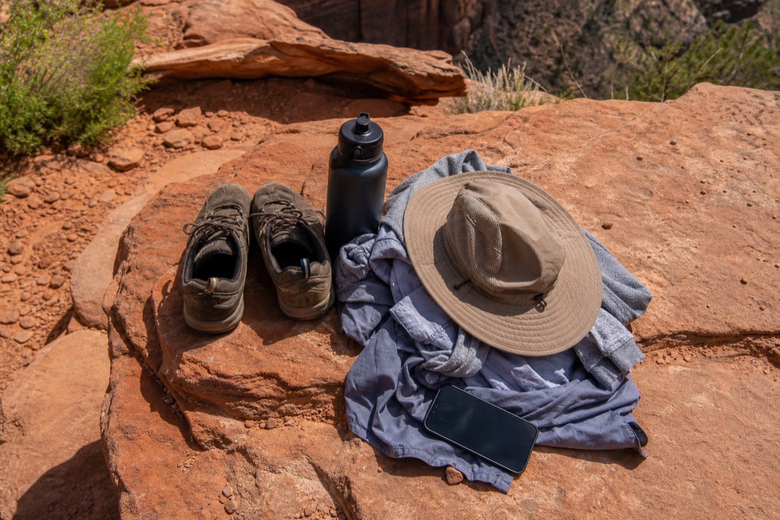 Flat lay of desert day-trip gear: closed-toe shoes, water bottle, light layers, sun hat, and a phone