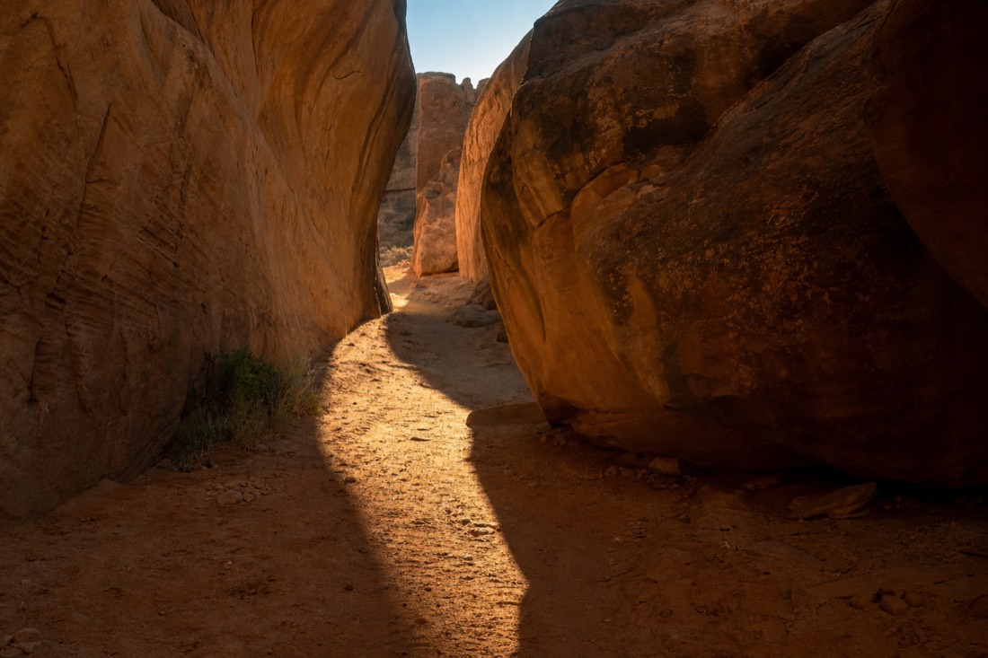 Early morning light on an empty slot canyon entrance path with long shadows across the sand