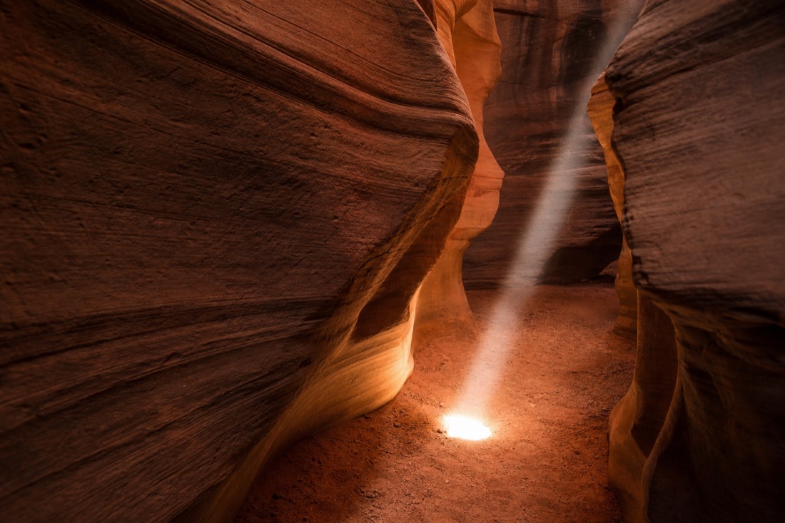 Thin shaft of light barely reaching the sand floor of a slot canyon in early spring