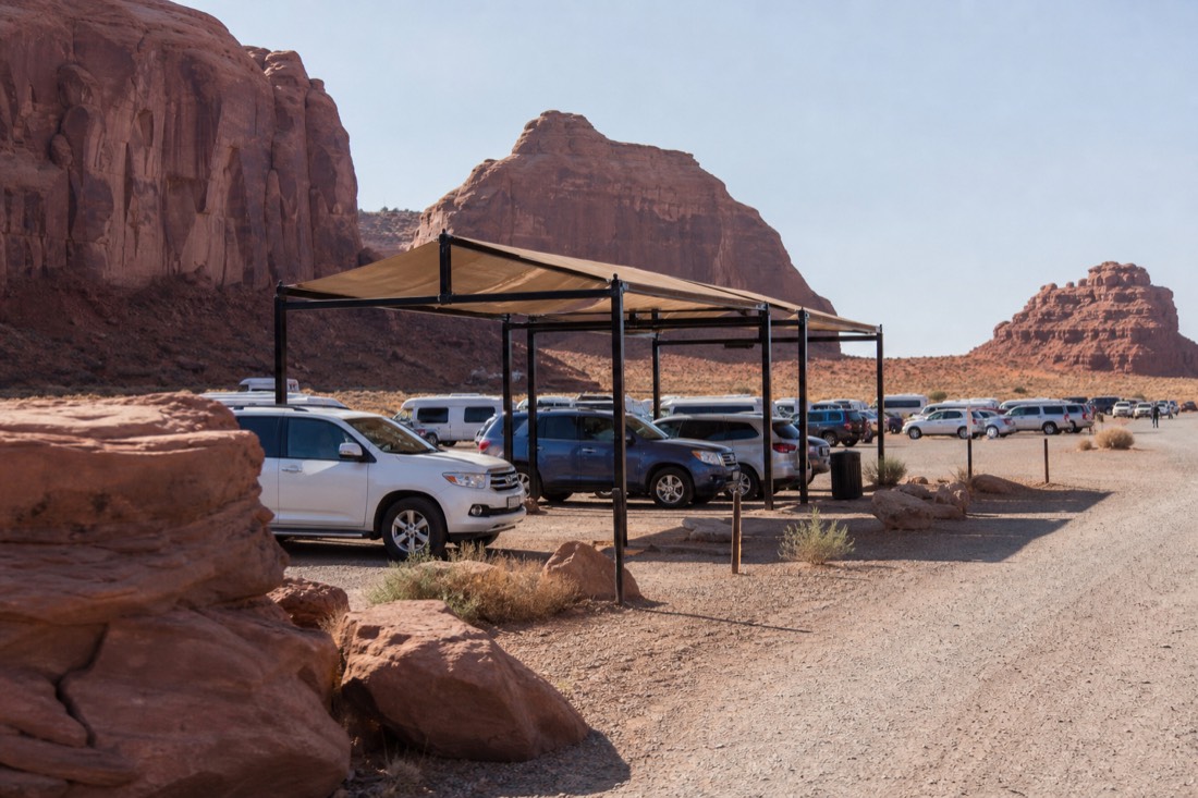 Busy desert check-in lot with several tour groups waiting under canopies in summer heat