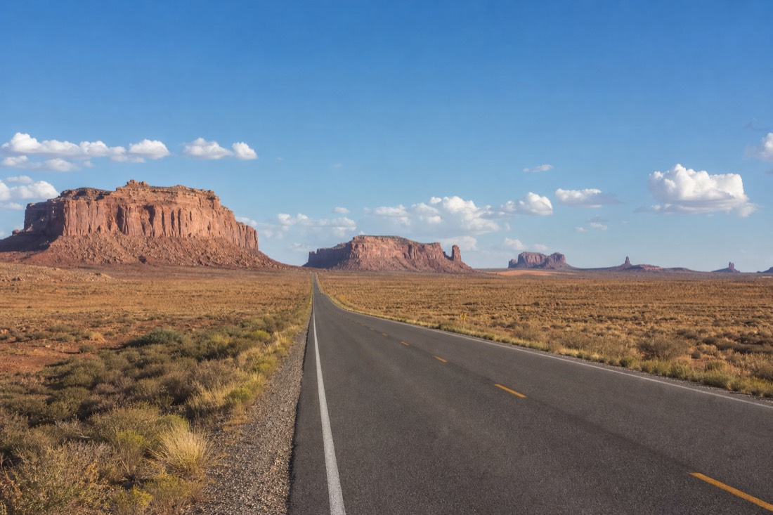 Long empty desert highway stretching toward distant mesas under a wide blue sky