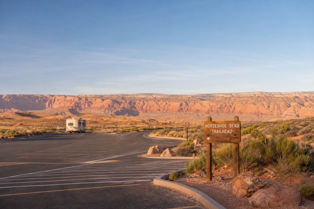 Wide paved Horseshoe Bend parking area with an RV lane and a trailhead sign at the edge of open desert