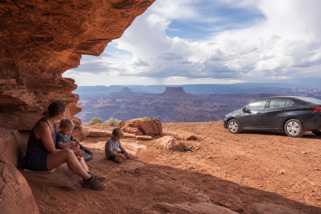 Family with young children resting at a shaded desert overlook beside a parked rental car