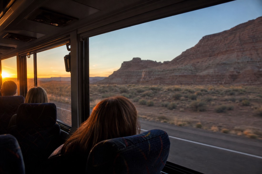 Interior of a tour coach on a desert highway with passengers watching sunrise through the windows