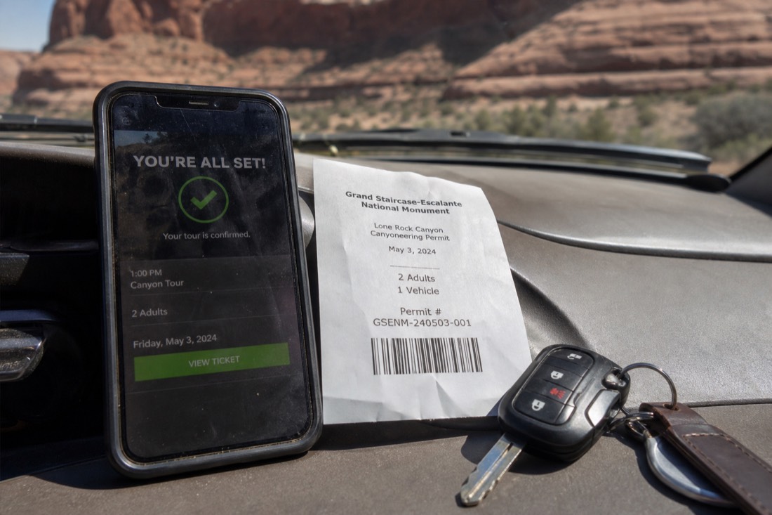 Phone showing a canyon tour confirmation beside a printed permit receipt and car keys on a dashboard