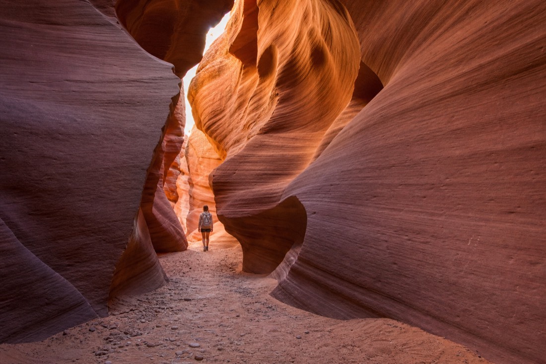Lone visitor in a spacious glowing slot canyon passage with rippled walls and soft light