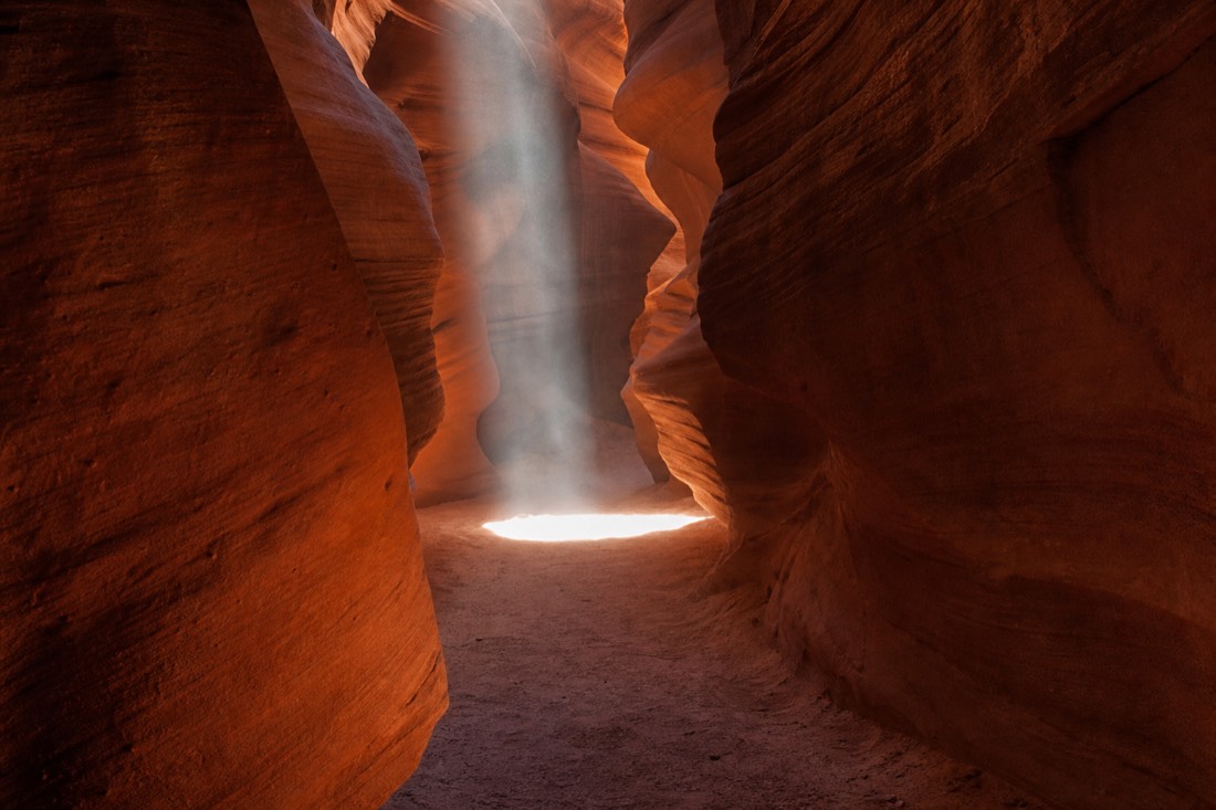 Midday light beam striking the floor of a busy slot canyon corridor as a guided group pauses to photograph it