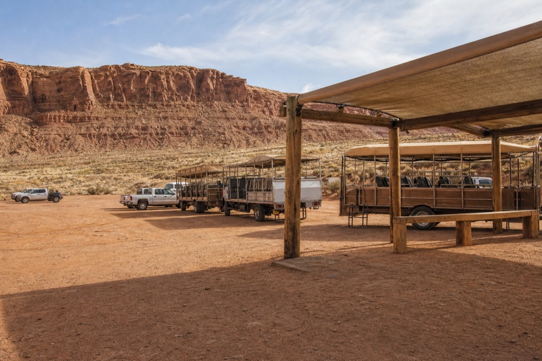 Tour trucks and a shaded check-in canopy on a dusty desert lot near Highway 98 outside Page, Arizona