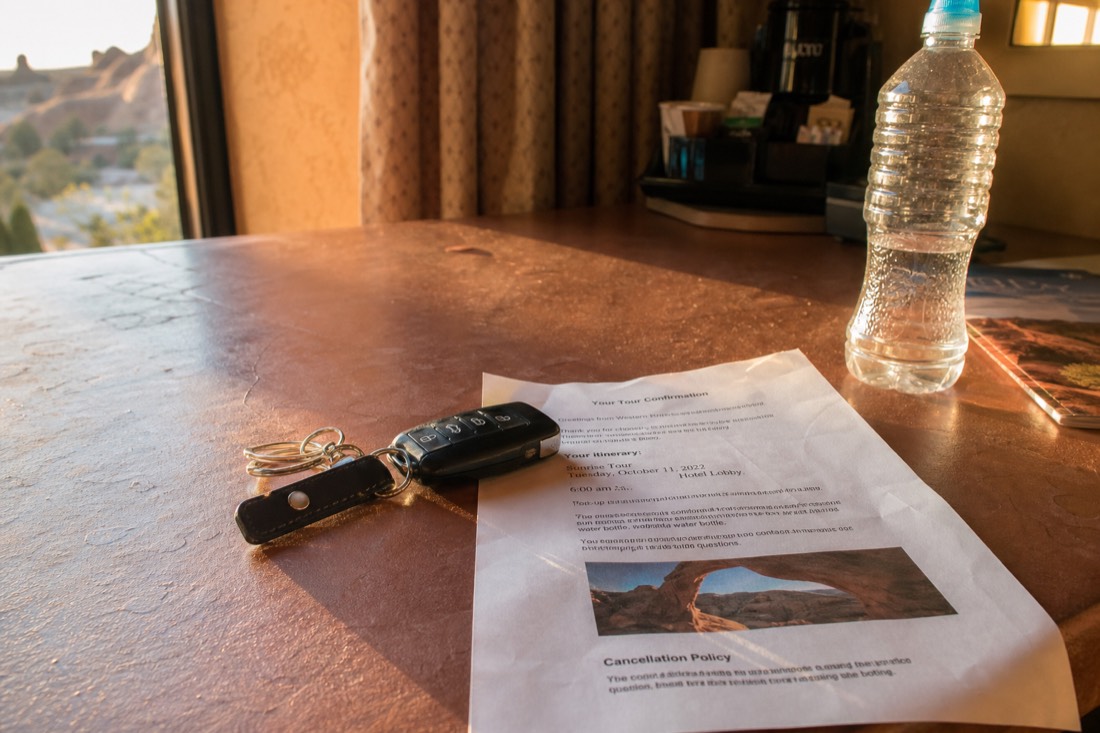 Car keys, a water bottle and a printed tour confirmation on a hotel desk in early morning light