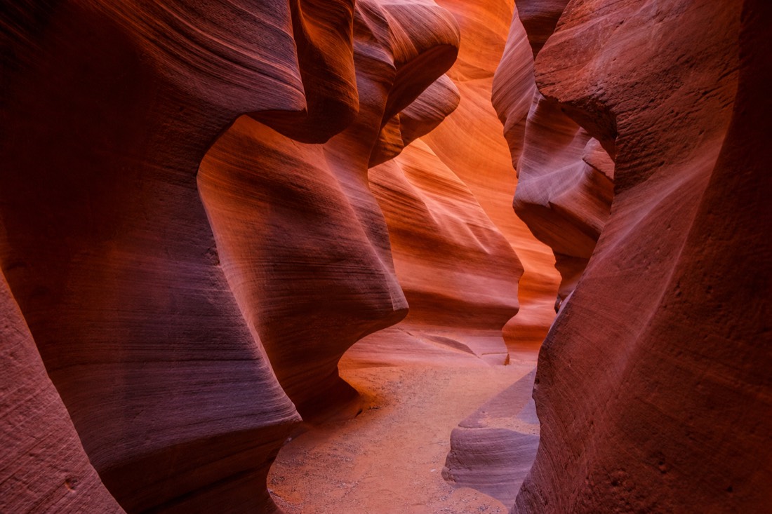 A shaft of soft light falling between the narrow curved walls deep inside Lower Antelope Canyon